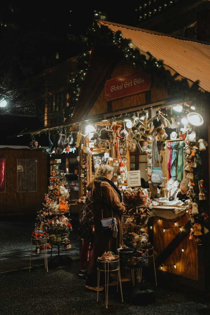 A woman bundled in warm clothes stands at a booth selling holiday gifts. It's lit up and festive looking. Pittsburgh holiday traditions