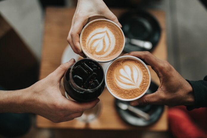 hands of three people of different colors holding cups of lattes from Pittsburgh coffee shops with latte art and cold brew coffee
