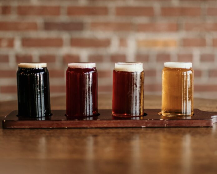 four glasses of beer on a wooden board in front of a brick wall with beer colors ranging from dark to light
