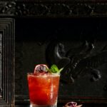 A strawberry fields cocktails sits in a rocks glass garnished with dehydrated blood orange slice and mint.