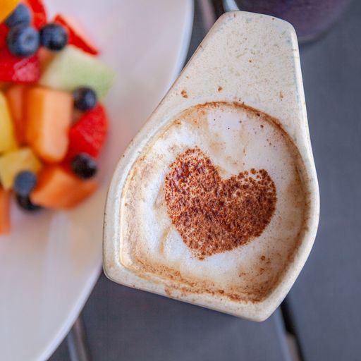 latte in a white mug with heart latte art next to a white plate with fruit salad