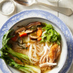 Asian-Inspired Chicken Noodle Soup served in a bowl, with lemon water, a spoon, and salt on the side