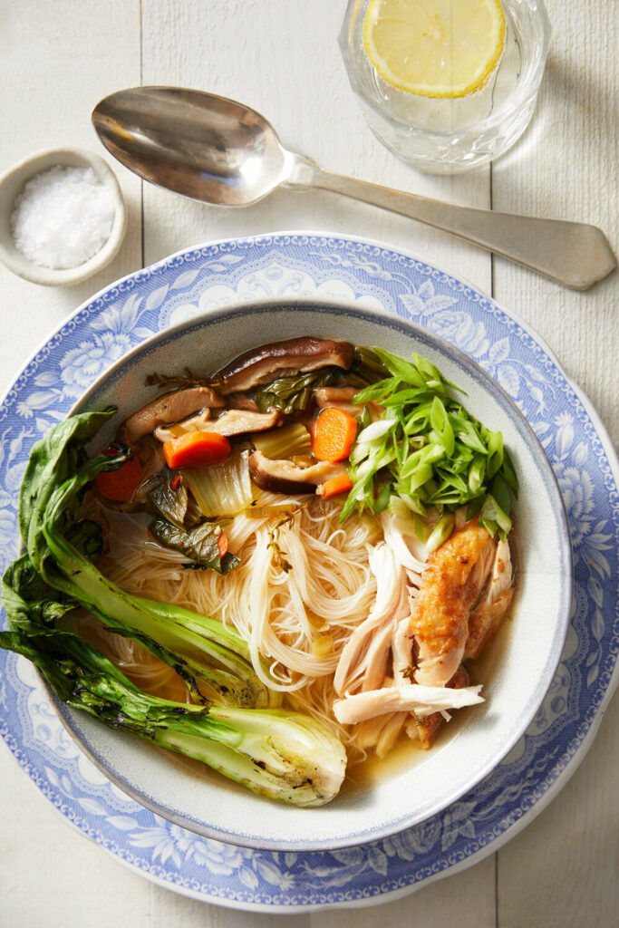 Asian-Inspired Chicken Noodle Soup served in a bowl, with lemon water, a spoon, and salt on the side