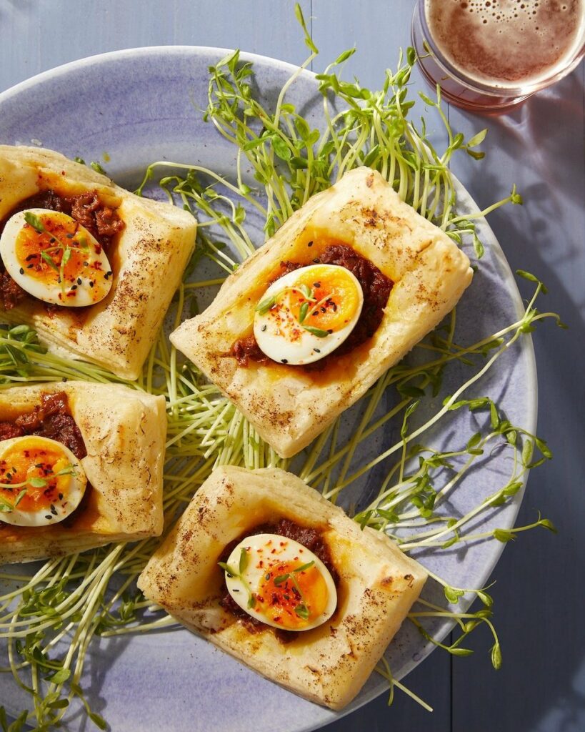 An aerial view of four Egg Masala Puffs on a grey plate with micro greens underneath.