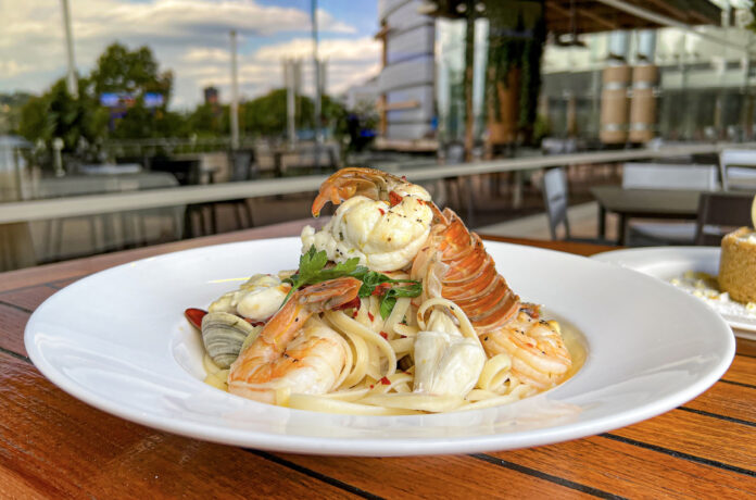 a dish of pasta with lobster and shrimp on a white plate set on a wooden table outside