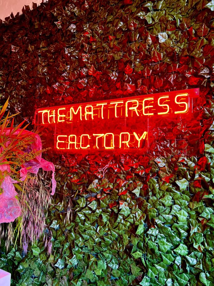 The Mattress Factory lit up in neon red letters against a green, leafy wall during their 2023 Trash Bash