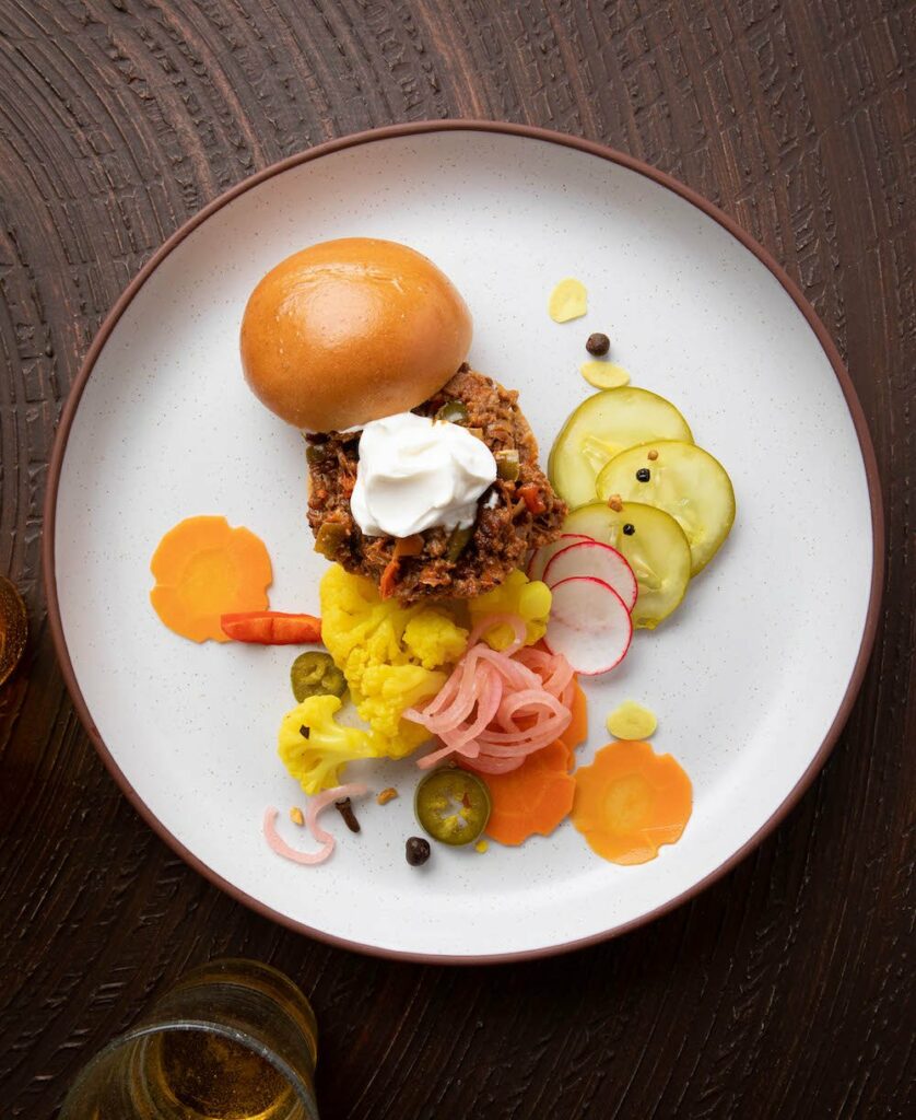 Deconstructed lamb sloppy joes with crème fraîche and a small bun on a white plate.