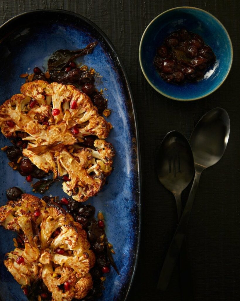 Cauliflower Steaks with Curry Leaf Oil and Red Wine Cherry Sauce sit on a blue plate to the left of the frame.