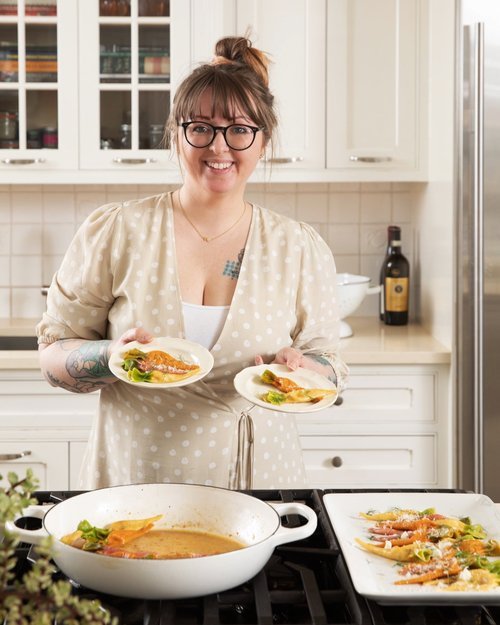 A mom holds two bowls of Rainbow Carrot Tortellini in a white kitchen.