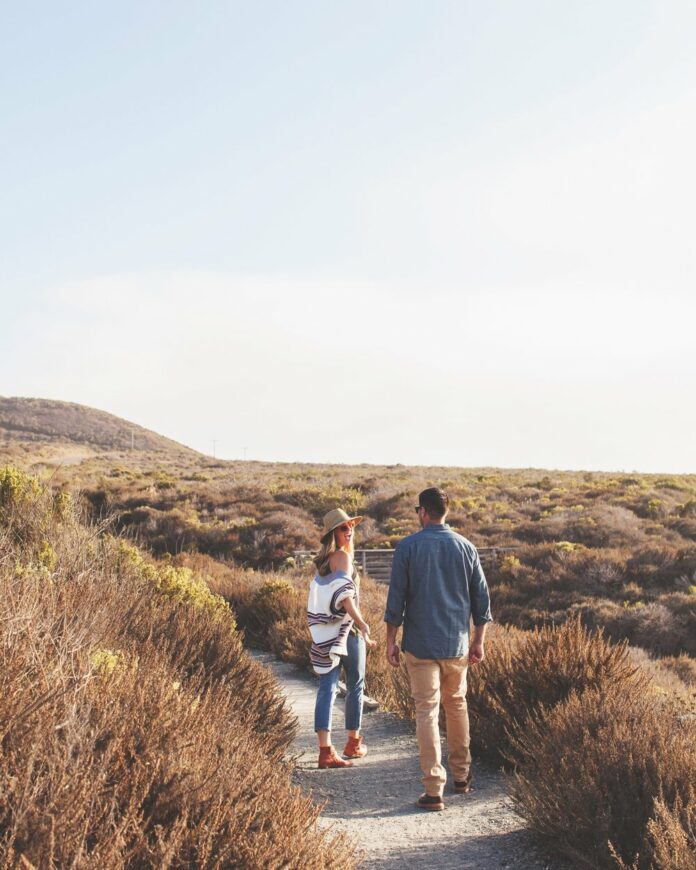 A man and a women walk through sand and brush in California.