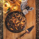 An aerial shot of a Smoky Blueberry Peach Crisp sitting in a cast iron pan, on top of a wooden cutting board.