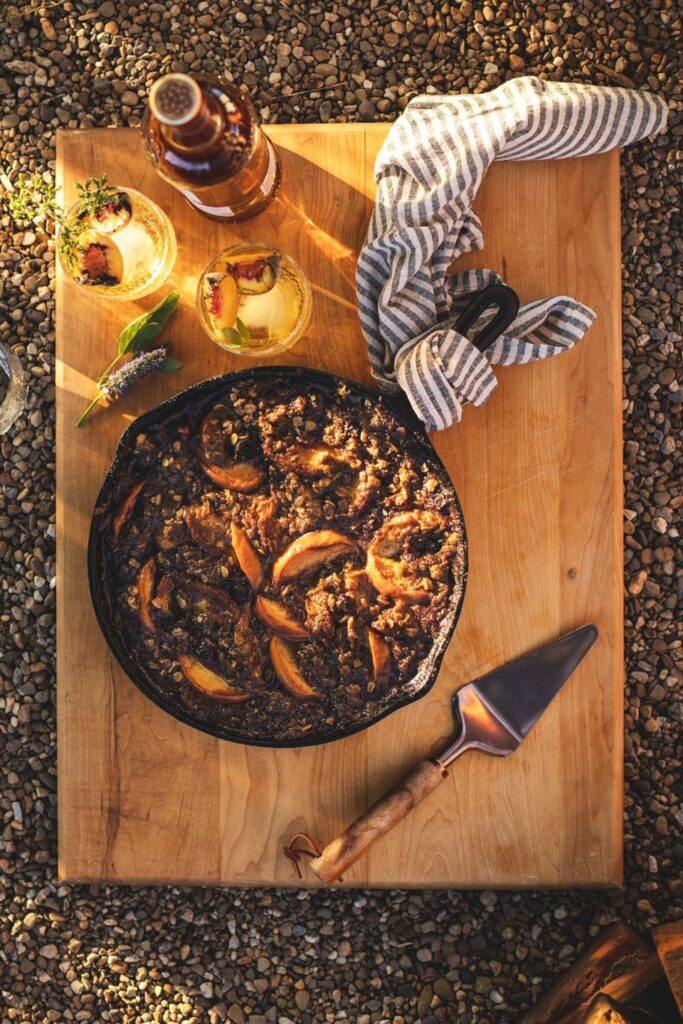 An aerial shot of a Smoky Blueberry Peach Crisp sitting in a cast iron pan, on top of a wooden cutting board.
