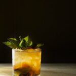 Deliciously refreshing grilled peach smash cocktail with fresh mint and a hint of citrus, served in a stylish glass.
