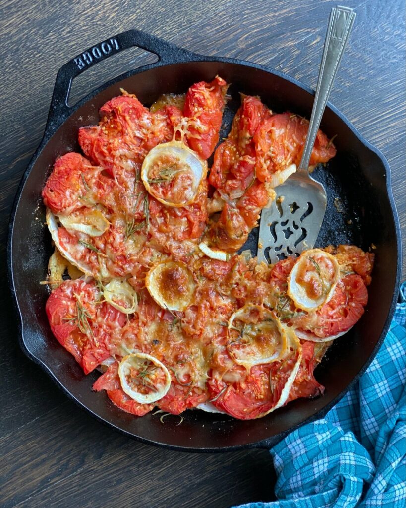 Summer Scalloped Tomatoes in a pan with a large spoon inside and a cloth on the side