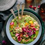White Bean and Cashew Hummus with Zhoug served in a bowl with three spoons inside and rose petal toppings
