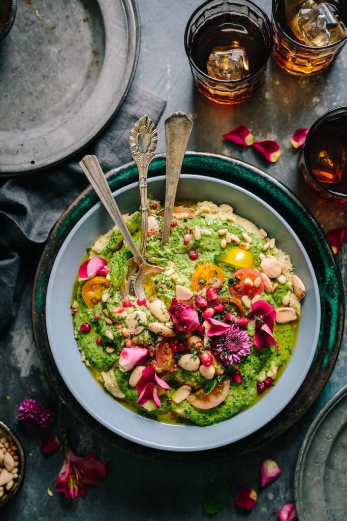 White Bean and Cashew Hummus with Zhoug served in a bowl with three spoons inside and rose petal toppings