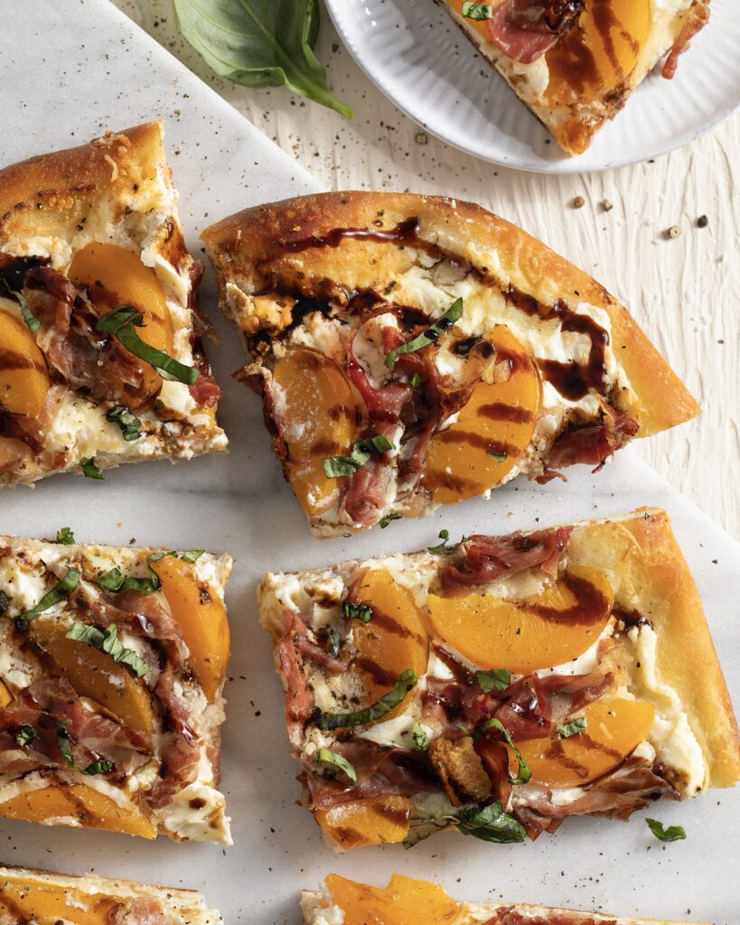 Four slices of Peach and Ricotta Pizza sit on a wooden background. They are orange and white in color and drizzled with a brown glaze.