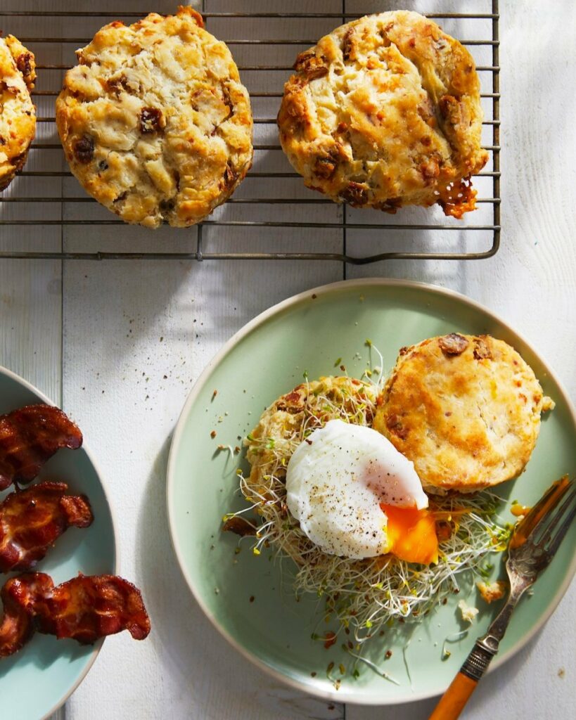 An aerial shot of Bacon, Blue Cheese & Date Biscuits, one sits on a plate while three others sit on a cooling rack. biscuits recipe