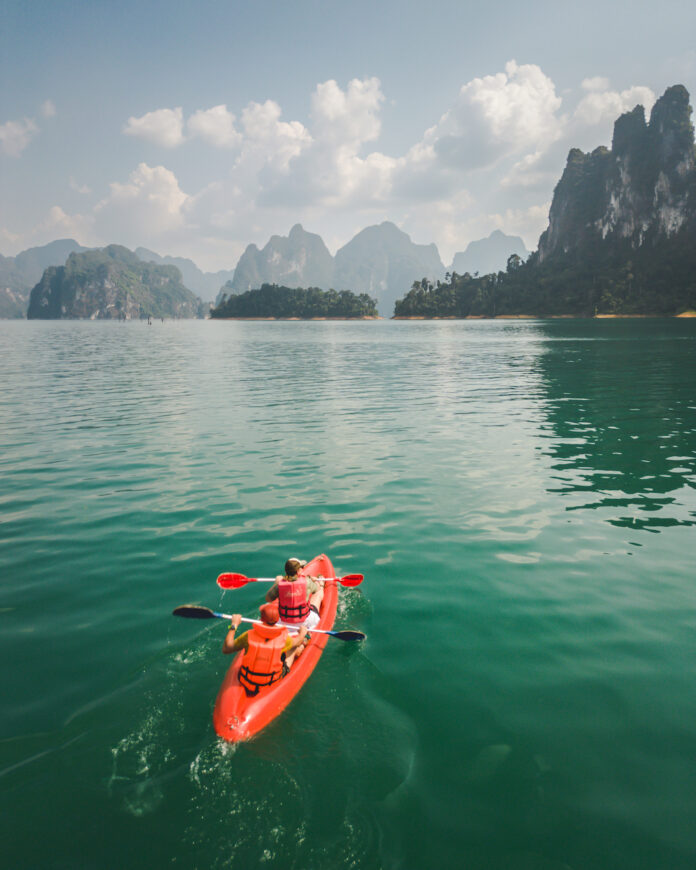 Two people in a red kayak paddle out into green/blue water in Thailand.
