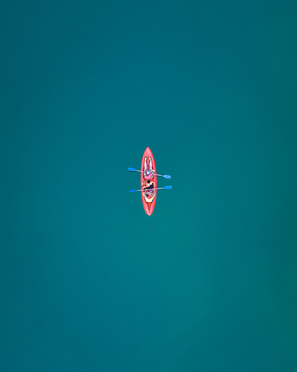 Two people sit in a pink kayak in the middle of turquoise water. 