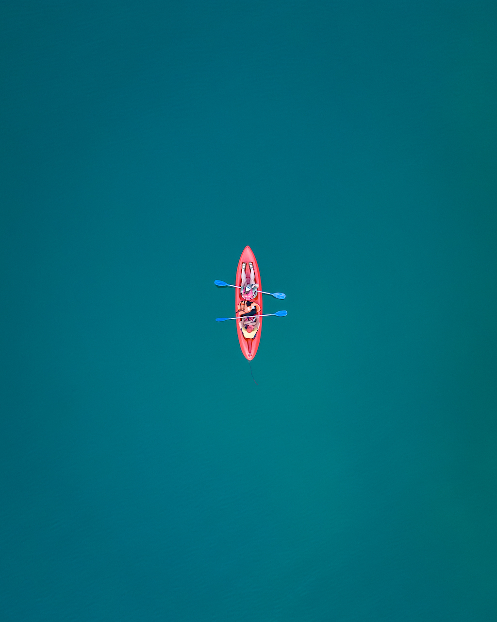 Two people sit in a pink kayak in the middle of turquoise water.