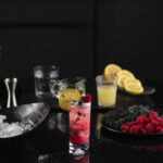 Wildberry Sparkler: A Refreshing Mocktail red in color, sits in a glass filled with berries and garnished with lemon.