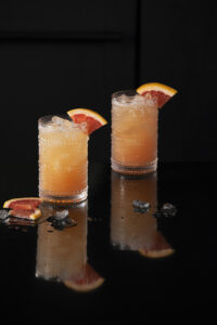 Two light orange greyhound cocktails sit in clear glasses garnished with grapefruit wedges. greyhound cocktail recipe