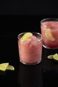 Two Frozen Cosmos, light pink in color, sit in glasses garnished by limes.