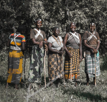Five Hadzabe Women stand together smiling in bright patterned garb