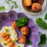 an arial view of a wide purple bowl with grilled peaches, whipped mascarpone and honey, garnished with fresh mint, and a smaller neutral colored bowl with grilled peaches
