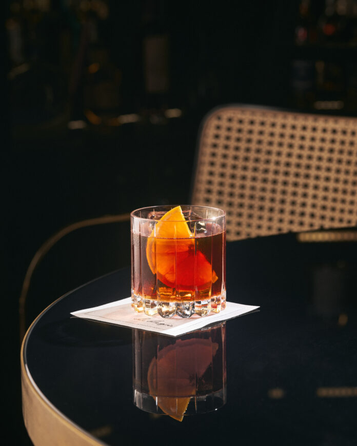 Cognac Negroni sits on a napkin on a mirrored top table. a cocktail worth traveling for. cocktails for traveling for