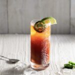 a look in photo of a tall glass with Bloody Mary mix and beer with a white back ground and lime wedges