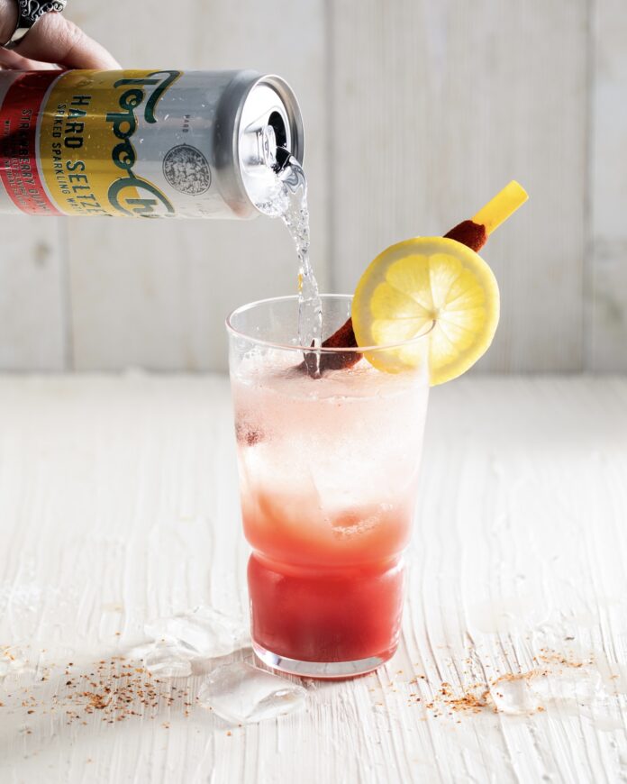 a clear glass with a white background with a pink Mexican Michelada cocktail being topped off with a can of hard seltzer
