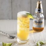 a tall glass with beer and lime with a bottle of beer in the background