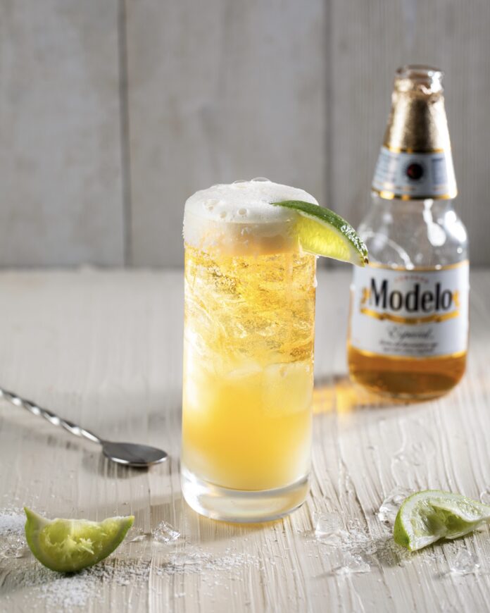 a tall glass with beer and lime with a bottle of beer in the background