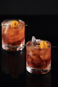 Two Negronis sit in rocks glasses garnished with orange peel. Classic Negroni Recipe