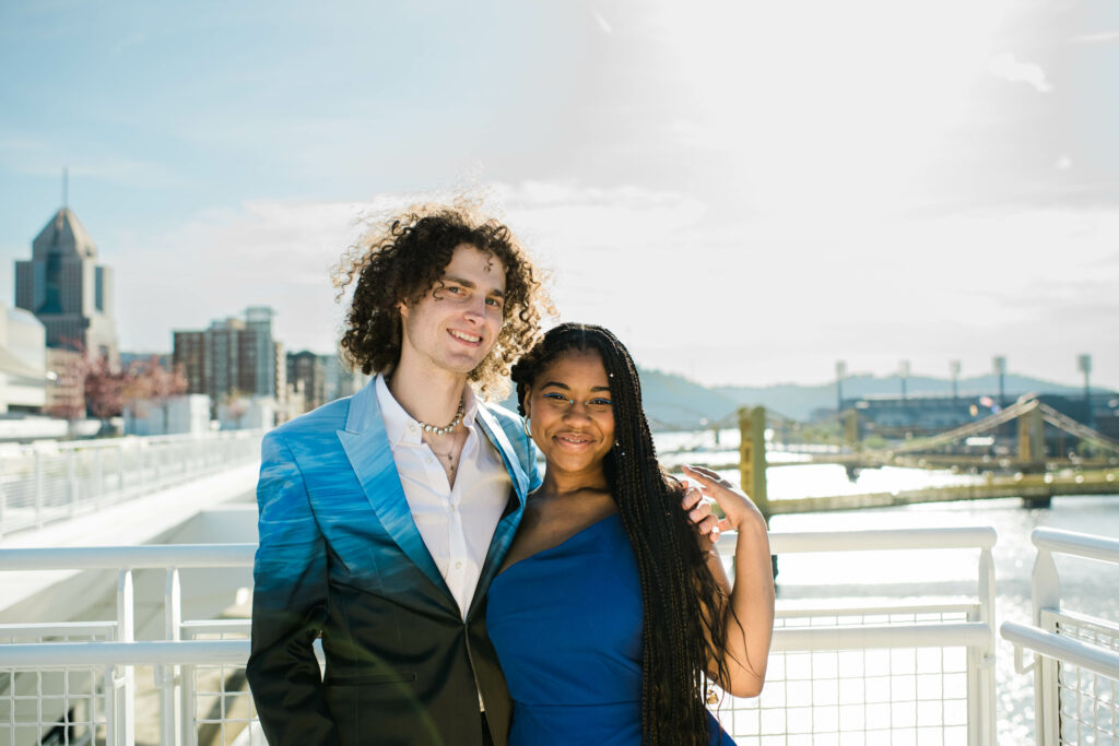 a couple dressed in blue cocktail attire standing on a rooftop overlooking the river. Riverlife's 2023 Party at the Pier