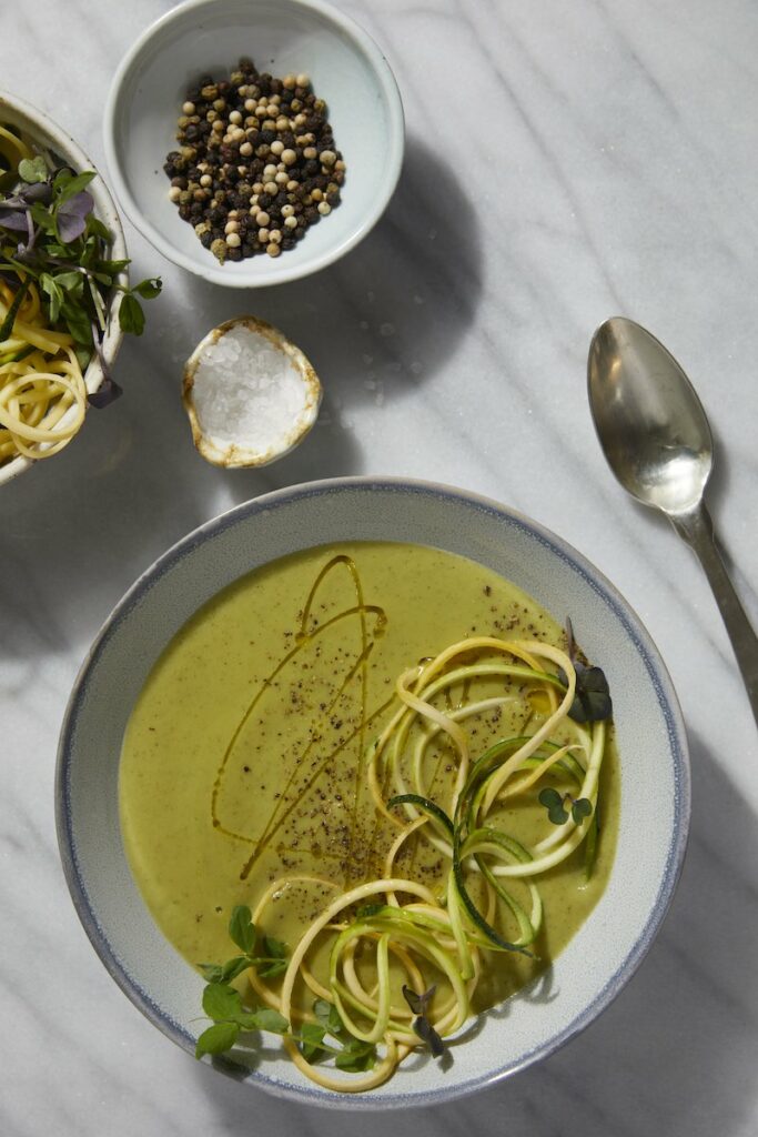An aerial shot of a green Zucchini Soup drizzled with oil and garnished with zoodles. Zucchini Soup reicpe