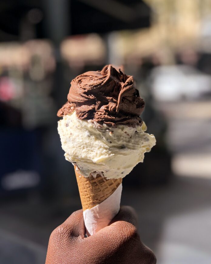 A hand-held double scoop of chocolate and vanilla ice cream in a sugar cone with a blurred out background