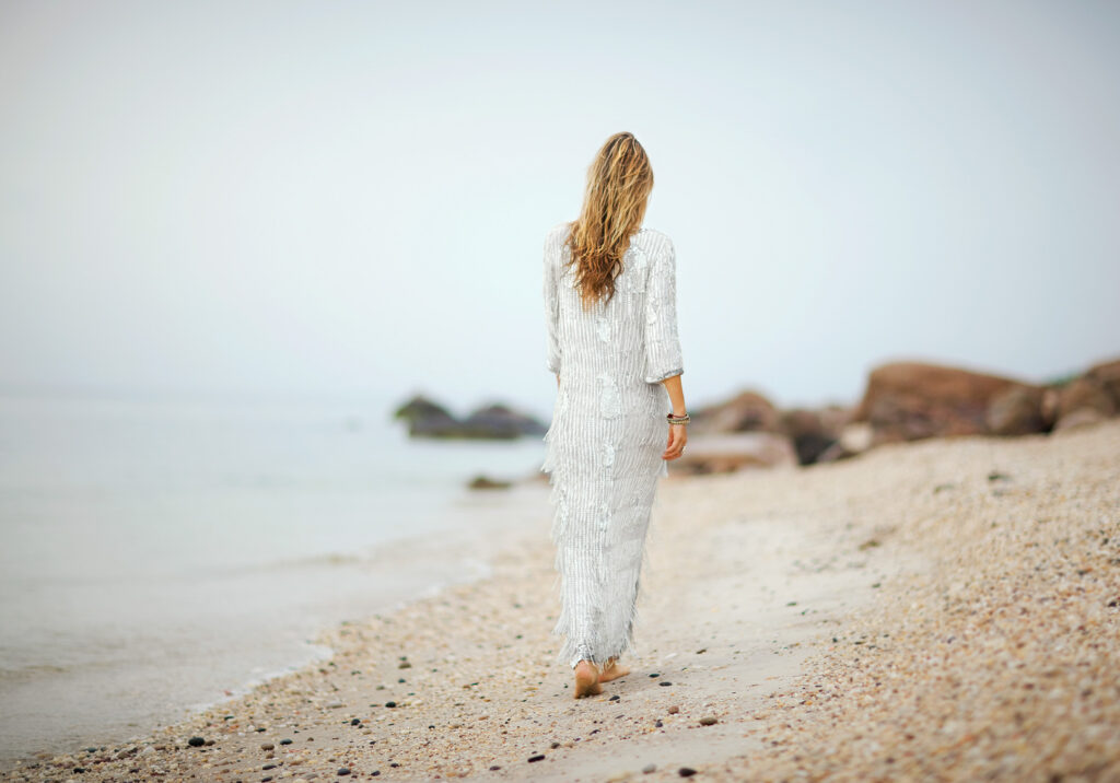 a woman with long blonde hair walks on a beach with her back to the camera
