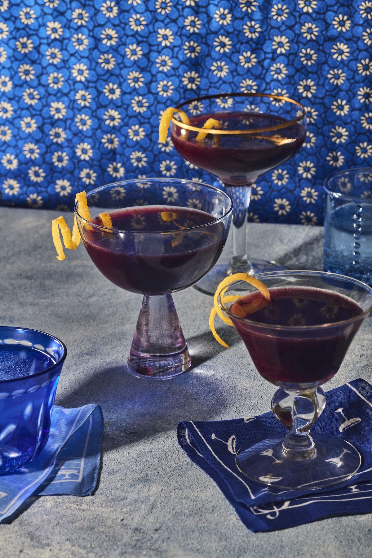 Three dark blue-purple cocktails in rocks glasses garnished with lemon twists. Blueberry Whiskey Sour Recipe