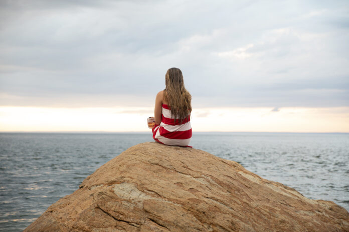 a woman sits on a rock looking out at the sea in the North Fork