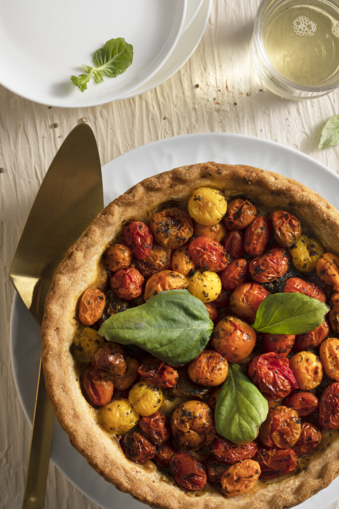 An aerial shot of a colorful tomato pie sitting on a white plate. It's garnished with basil. Tomato Pie Recipe