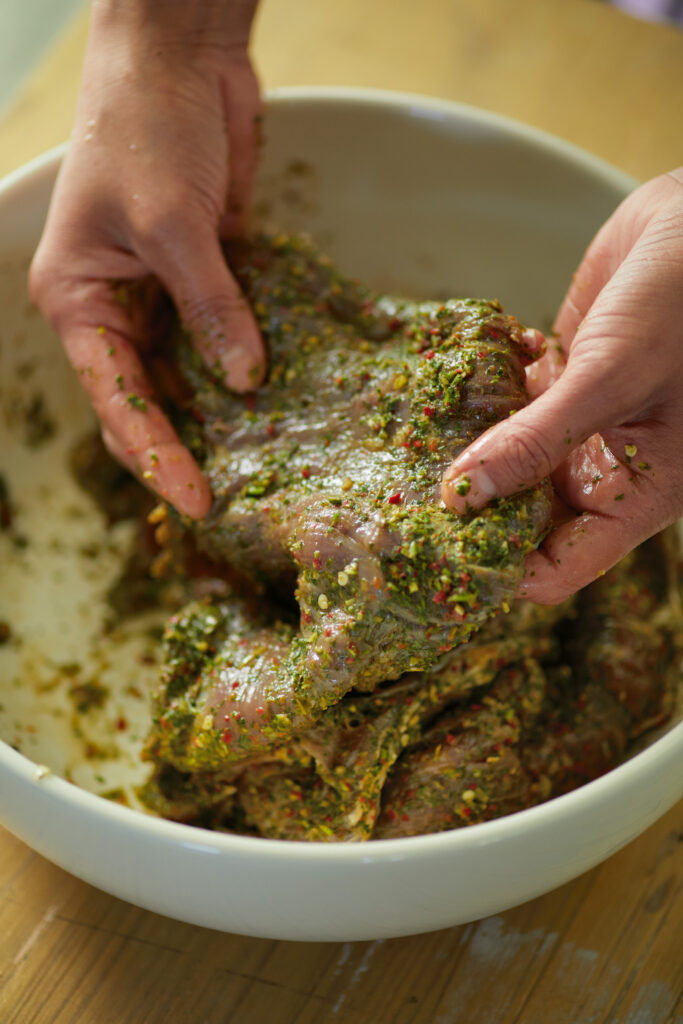 A pair of hands runs Arrachera Verde on raw chicken. Arrachera Verde Recipe in a white bowl.
