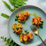 Four bacon wrapped scallops with fruity mango pineapple salsa sits on a blue plate.