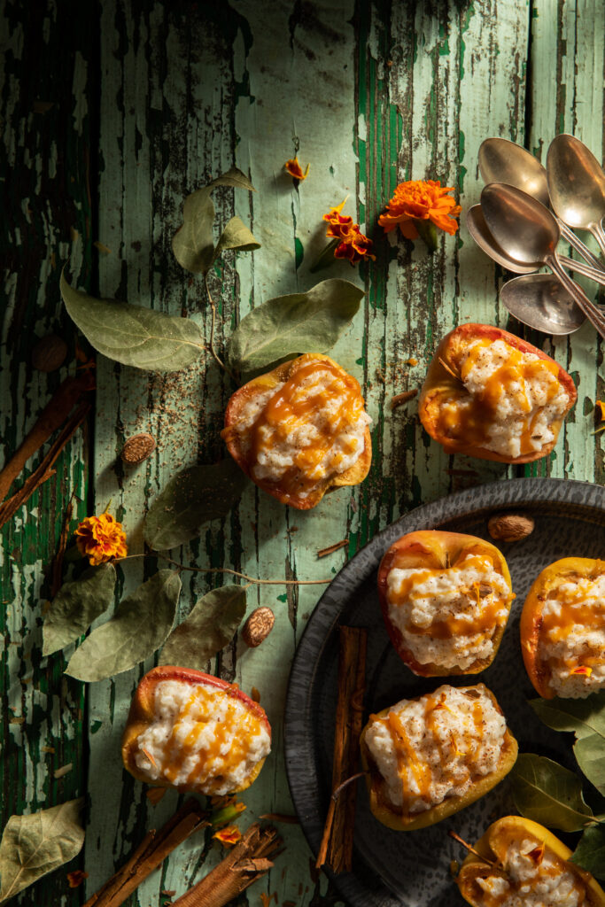 Flat-lay image of apples filled with caramel baked rice pudding on a weathered table. Caramel Apple Rice Pudding Recipe