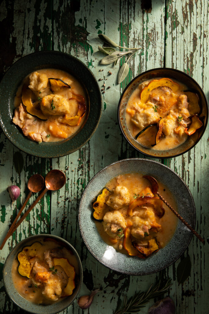 Flat-lay image of chicken and dumplings in small bowls on a weathered table.