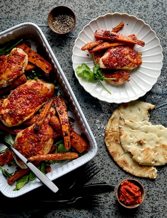 A white casserole dish sits with carrots and chicken covered with a redish glaze. To the rights sits a plate with the chicken and carrot recipe.