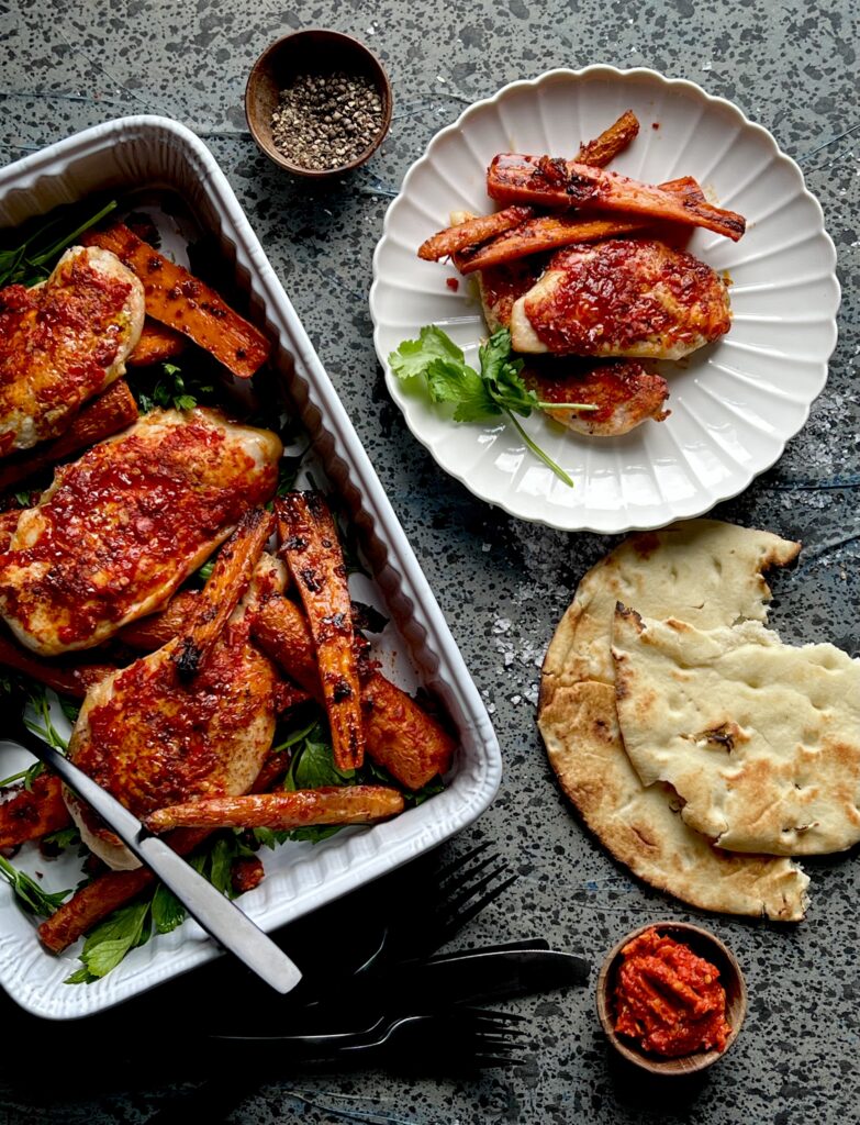 A white casserole dish sits with carrots and chicken covered with a redish glaze. To the rights sits a plate with the chicken and carrot recipe.