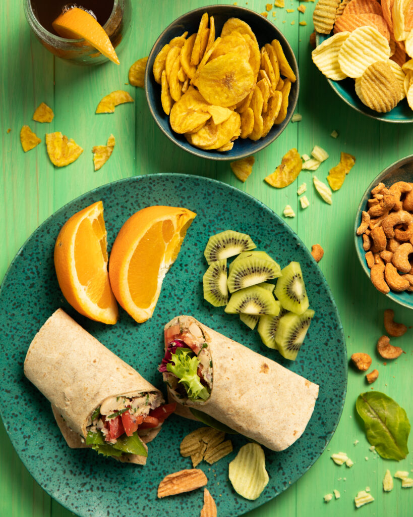 White Bean Tuna Salad Wraps sit on a green plate with two orange slices, and a few pieces of kiwi.